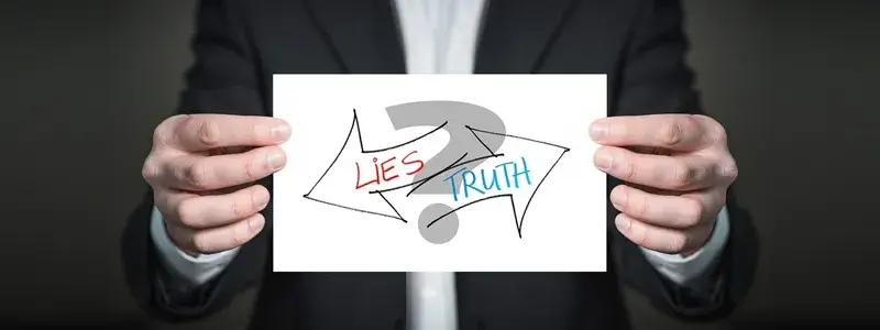 LIESとTRUTHの矢印が描かれた紙を持つ男性の写真。アップルワインに関する誤解と真実を象徴するイメージ