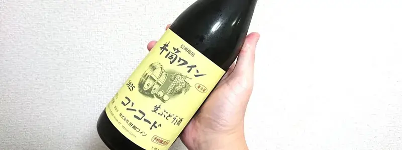 青木周作商店で購入した井筒ワインの生ぶどう酒コンコードを手に持って撮影した写真