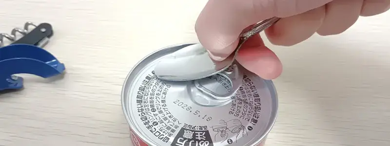 スプーンや硬貨を使って缶詰のフタを押し広げて開けている様子