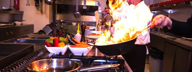 プロのシェフがフライパンでフランベし、炎が立ち上っている。ワインのアルコールを飛ばす加熱イメージを示唆